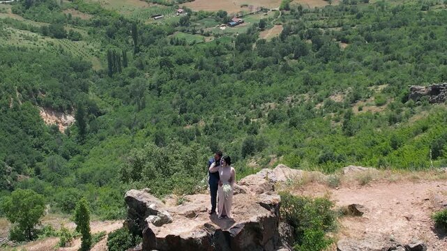 Brave wedding just married couple standing on mountain peak rock with beautiful aerial view of picturesque rural landscape