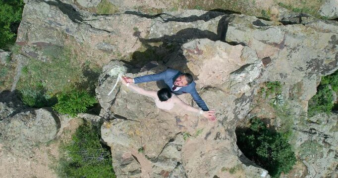 Bride and groom spread hands celebrating standing on natural mountain peak rocky landscape captured from above