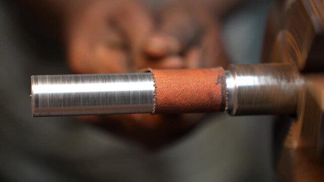 View of a metal rod rotating on a lathe machine with a worker using sandpaper for polishing in a workshop in Kushtia, Khulna Division, Bangladesh.