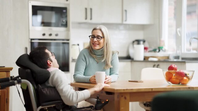 Supportive mother and her son with a physical impairment enjoying a warm conversation in the kitchen. Loving family relationship and daily life