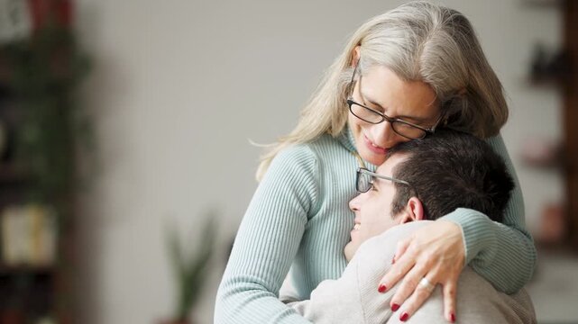 Caring mother lovingly embracing her adult son living with a physical condition. Beautiful moment showing unconditional love and family support