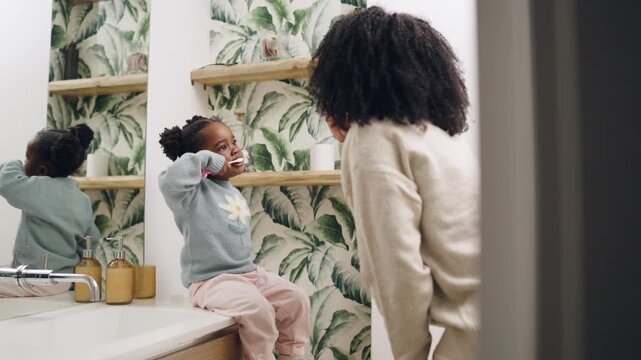 Young girl sitting on a bathroom counter learning about dental hygiene and oral care from her mother. Caring parent teaching her kid