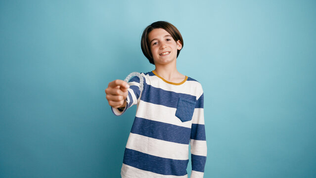 Young boy smiling and presenting a clear aligner for tooth straightening against a blue background, focusing on dental care