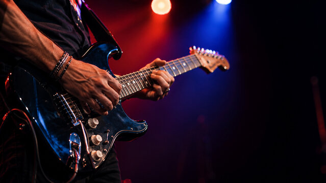 Guitarist hands playing electric guitar under colorful concert lights