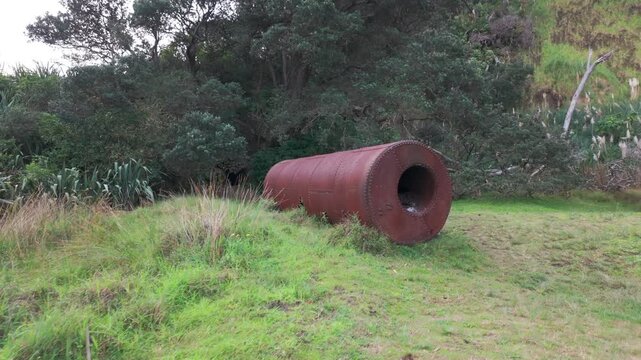 A large, rusty, cylindrical tank lies on a grassy hillside in KareKare, Auckland, New Zealand., New Zealand. The tank is an old mining relic.