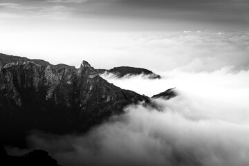 Dramatic black and white landscape of rugged mountain peaks rising above a thick, flowing sea of...