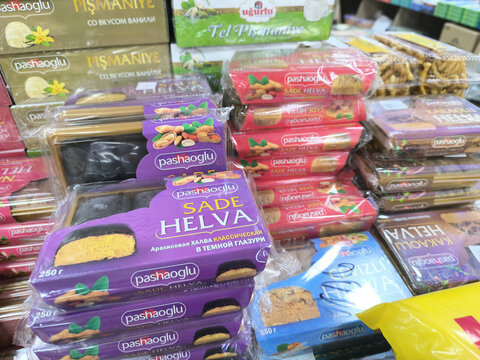 Various packaged Turkish halva sweet snacks in a grocery store display. Assorted traditional Middle Eastern confectionery desserts on a retail shop shelf. Food culture and regional treats.
