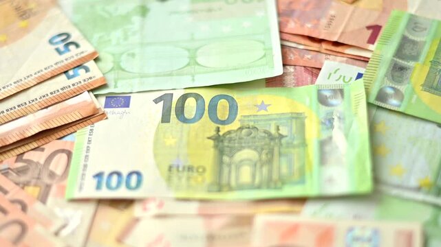 Slow zoom into pile of euro banknotes focusing on one hundred euro bill lying among fifty and twenty bills.
