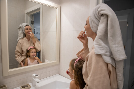 A beautiful adult woman and her daughter are caring for their lips in the bathroom at home. The child is playing and applying lipstick. Family hygiene. Real photo.