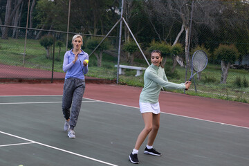 Obraz premium Two female partners practicing on park court in sneakers, holding racket and ball, copy space