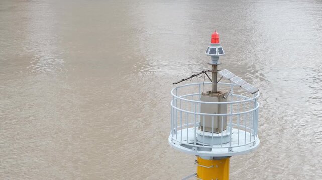 A river navigation beacon with solar-powered marine warning light above muddy river or water channel in Ningbo, China. Industrial waterway safety infrastructure used for navigation, monitoring