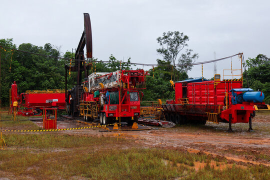 Tanjung-Indonesia May 17, 2026 ​A comprehensive view of an onshore petroleum extraction site featuring an active pumpjack unit, mobile workover rig truck, and technical container facilities on a muddy