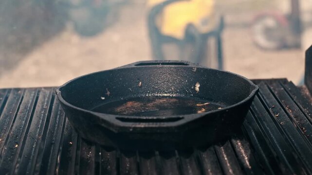 Burger patty with cheese expertly flipped in cast iron pan on grill during cooking process.