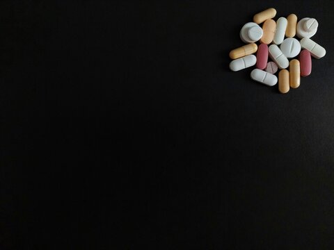 Assorted pills, tablets, capsules isolated on black background with copy space for drugs, medications, prescription medicines, medical treatments, vitamins, pharmaceuticals, and healthcare concepts.