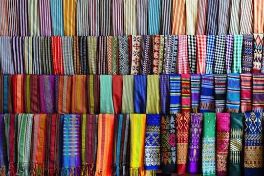 Traditional handmade colorful ethnic brocade fabrics and woven scarfs with geometric patterns displayed in rows at souvenir market in Vietnam