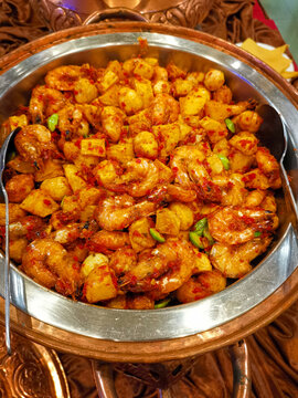 Close up of traditional Indonesian sambal goreng udang kentang with petai or stink beans, served hot in a metallic catering chafing dish at an event.