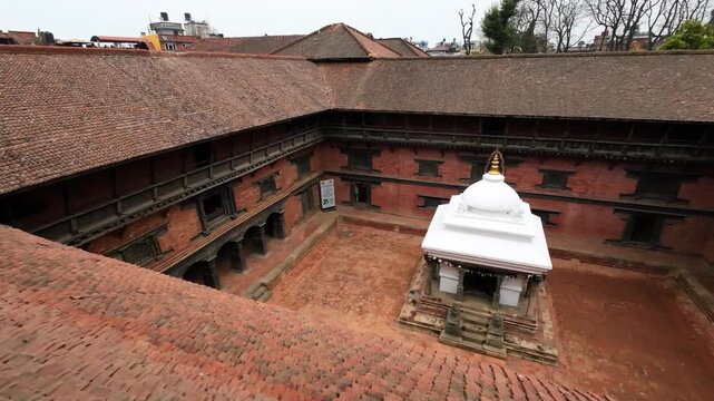 View of a traditional Newari courtyard with red brick architecture and a white stupa in Nepal.