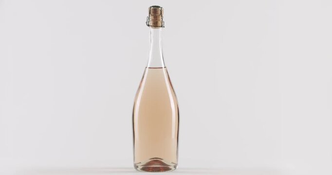 Elegant glass bottle filled with delicious pink sparkling wine rotating in slow motion. The unlabeled container is perfect for showcasing luxury alcoholic beverages for celebrations and parties.