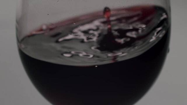 Deep red wine swirling in a crystal clear glass, creating beautiful waves and ripples on the surface against a plain white background, highlighting the rich color and elegant movement