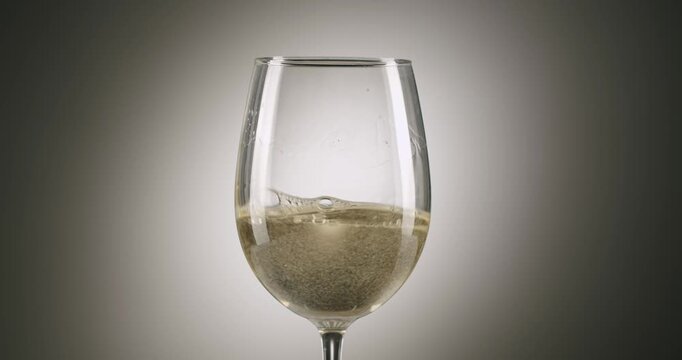 Elegant white wine swirling in a transparent glass, creating mesmerizing circular patterns and gentle waves. The graceful movement against a subtle grey background highlights the liquid's texture