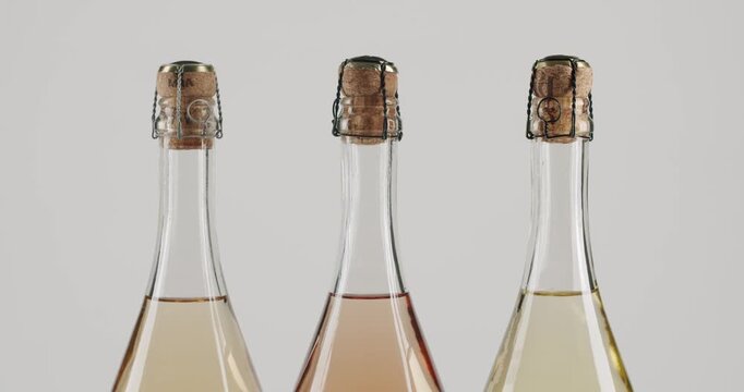 Three different sparkling champagne bottles, including white and rose, slowly rotating on a clean white background, showcasing the cork, wire cage, and elegant shape for celebration