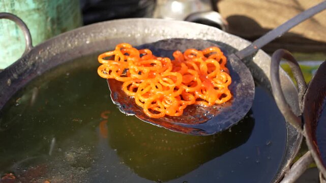 View of traditional orange jalebi sweets being deep fried in large metal pans with bubbling oil at a street food stall in Nepal.