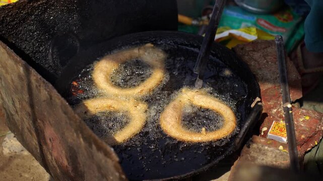 View of traditional ring-shaped sel roti being deep-fried in a large pan of bubbling oil at a street food stall in Nepal.