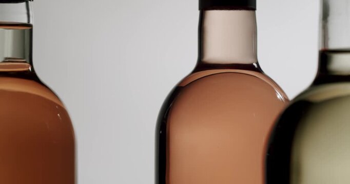 Close-up of three elegant wine bottles spinning on a white background, showing rose, white, and red wine with ample copy space for text. The sophisticated rotation highlights the different colors.