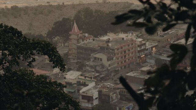 Elevated view of a small town in India during a heavy rainstorm with tree branches in the foreground, showing the moody atmosphere of the monsoon season and daily life continuing