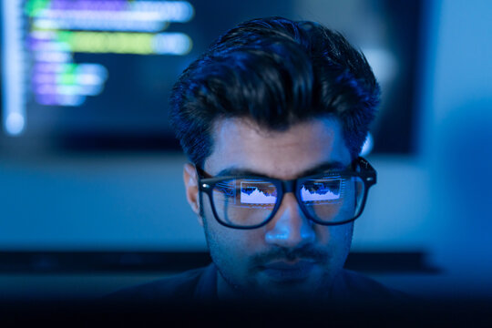 Close-up of male programmer wearing glasses with reflection of financial data chart and coding, Concept of data analysis, software engineering, cybersecurity, stock market trading and business network