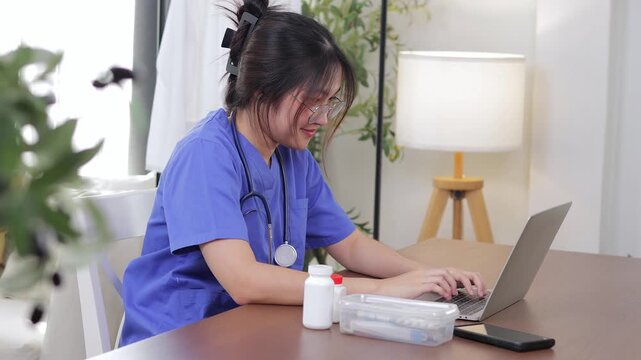 Female doctor providing online consultation via laptop at home, wearing blue scrubs. Concept of telemedicine, remote healthcare, and modern digital medical service in new normal lifestyle.