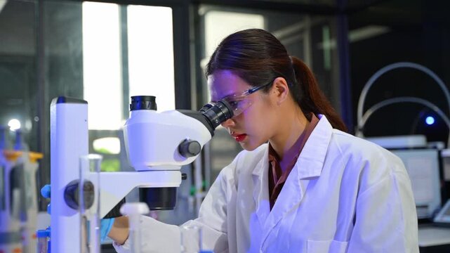 Female Scientist Using Microscope in Laboratory with Scientific Equipment and Glassware