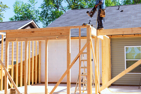 Worker builds wooden frame on top of home ladders tools are nearby as work begins.