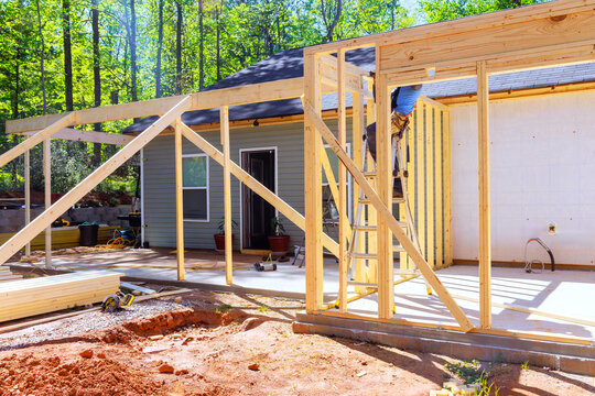 Workers install wooden beams for home extension in wooded area during trusses frame