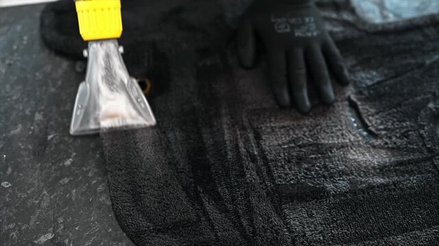 Professional worker deep cleaning black car floor mat with vacuum extraction tool.