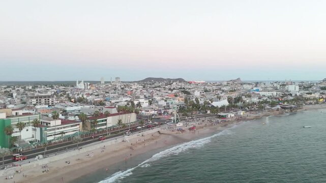 Vista a&eacute;rea de zona urbana costera en el Pac&iacute;fico mexicano, mostrando la multitud en la playa as&iacute; como el tr&aacute;fico en el malec&oacute;n, ideal para videos de viajes y estilo de vida 