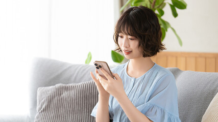 リビングのソファでスマートフォンを使う女性, Woman Using Smartphone on a Living Room Sofa © Trickster*