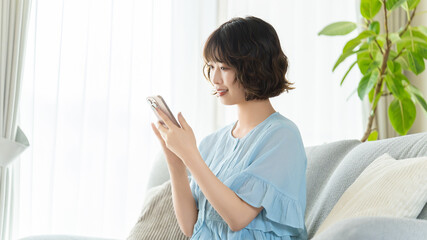 リビングのソファでスマートフォンを使う女性, Woman Using Smartphone on a Living Room Sofa © Trickster*