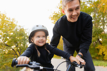 Fototapeta premium Happy Father teaches young caucasian daughter to ride bicycle in park, child girl smile and funny