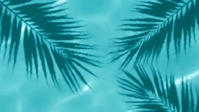 Dark palm leaf shadows cast on the bright turquoise rippling water of a swimming pool