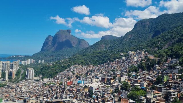 Wide panoramic view of Rocinha favela in Rio de Janeiro, Brazil, with tightly packed hillside homes and dense urban structures on a sunny day, contrasting with modern high-rise buildings