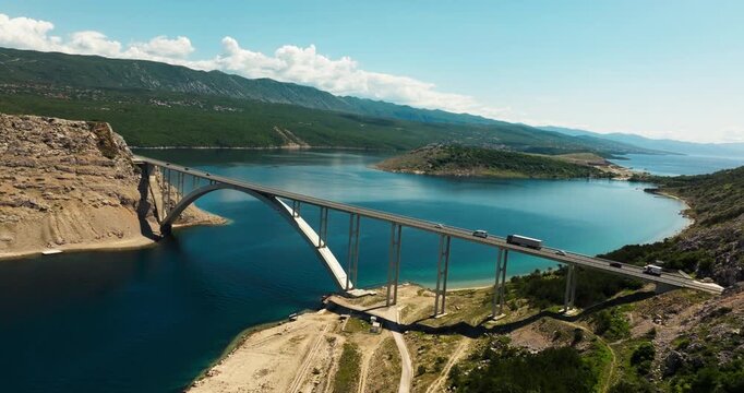 Krk Bridge spanning turquoise Adriatic waters in Croatia with vehicles crossing between the mainland and Krk Island on a sunny summer day.