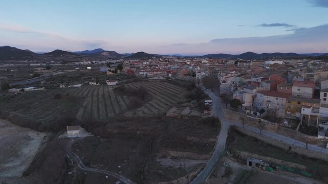 Drone timelapse flying above rural farmland and vineyards toward Bullas town during colorful sunset in Murcia Spain.