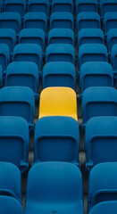 Obraz premium A solitary yellow theater seat stands out among rows of blue seats in a crowded auditorium or stadium symbolizing individuality and uniqueness in a sea of conformity.