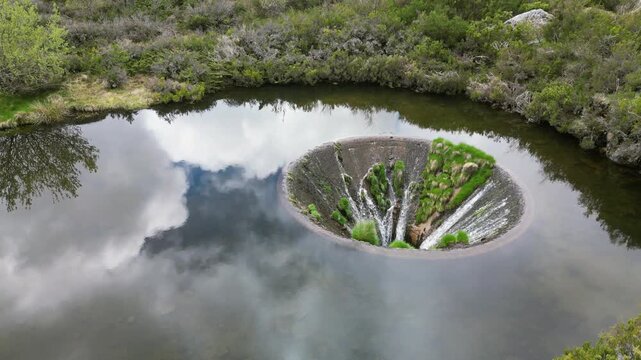 Aerial drone footage of Cov&atilde;o dos Conchos, Portugal: mountain lake with a unique circular spillway surrounded by Serra da Estrela landscape. Ideal for travel and nature projects.