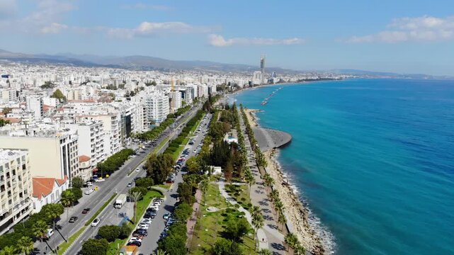 Aerial view of Limassol cityscape and coastline with turquoise sea and parked cars on the promenade.