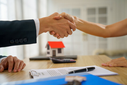 Handshake agreement real estate contract mortgage house buyer seller confirm deal at office desk with agent signing contract document beside pen and calculator joyful closing and strong trust