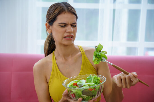 Woman salad disgust picky lettuce tomato young adult frowns holding chopsticks on sofa at home resisting healthy vegetarian meal with reluctant mood