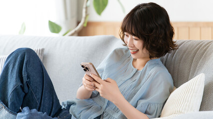 ソファにもたれてスマートフォンを使う女性, Woman Using Smartphone While Relaxing on a Sofa © Trickster*