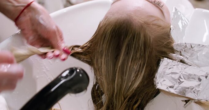 Salon highlighting. Hairstylist treatment. Skilled woman hands rinsing shampoo providing professional service after coloring procedure.